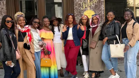Jemima Antwi A group of black women smiling and standing together for a group photo in front of a hotel.