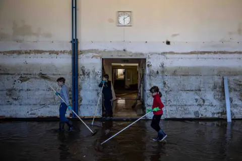 Crianças da EPA com paus limpando escola inundada