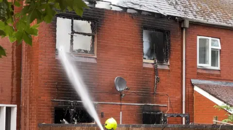 A two-storey house that has been blasted with water. Its roof has caved in because of the fire and the window