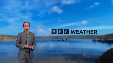 BBC Scotland's Calum MacColl presents the upwind  wearing a grey suit   and necktie  and greenish  shirt. 