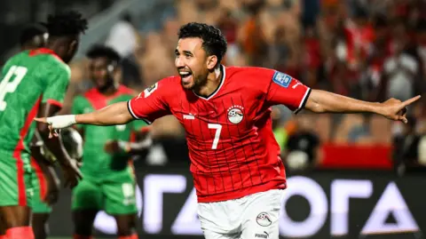 Egypt forward Trezeguet smiles and wheels away with his arms wide in celebration after scoring a goal