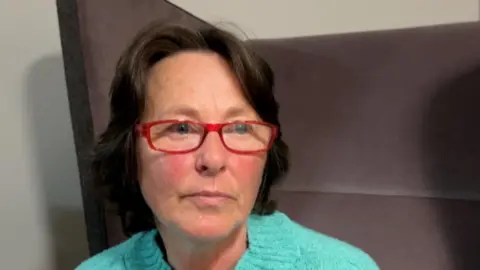 Middle aged woman in green jumper and red rimmed glasses