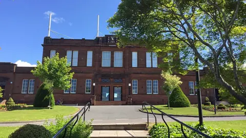 A large sandstone building with a flat frontage and lawns in front of it
