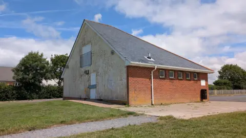 A picture from outside Tews Lane Pavilion. It is a building at the centre of a grassy area.