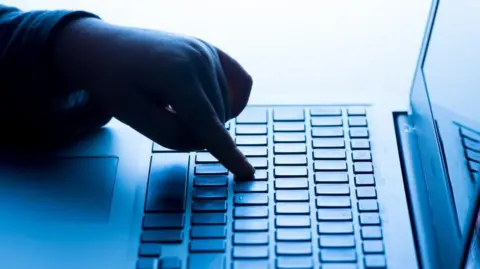 A child's finger is typing on a laptop that is shaded blue from lighting. 