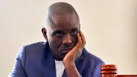 Erias Lukwago, in a navy blue jacket and white shirt appears in the dock