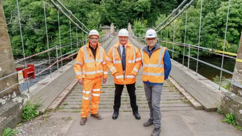 Durham County Council (L-R) Lee Jackson, project manager at VolkerLaser with John Shuttleworth and Alan Patrickson fromm Durham County Council. They are standing on the bridge and are wearing orange hi-vis jackets.