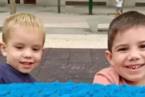 Rubén and Izan Matías, two young boys, are stood outside and are smiling at the camera. The photo only shows their heads and shoulders