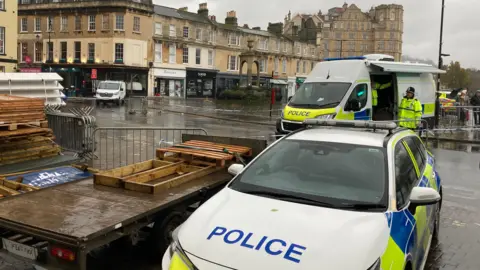 The police presence at Terrace Walk in Bath. There is police tape around the pedestrianised pathways, a police van and a police car. 