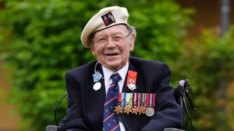 Albert Lamond smiling at the camera. He is wearing a white military hat and a blue blazer with a collection of medals on the upper right chest.