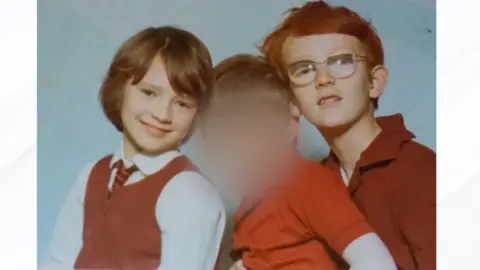 Handout A photo of three young children - the face of the middle child has been blurred. The child on the left is Jill Harris and the child on the right is John Harris. They all wear red school uniforms.