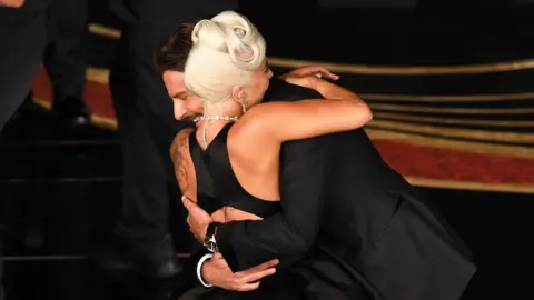 Getty Images Lady Gaga and Bradley Cooper embracing in smart, black outfits at the Oscars