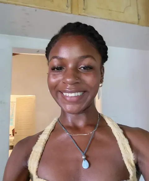 Arthouse Jersey A black woman with a blue pendant necklace, smiling