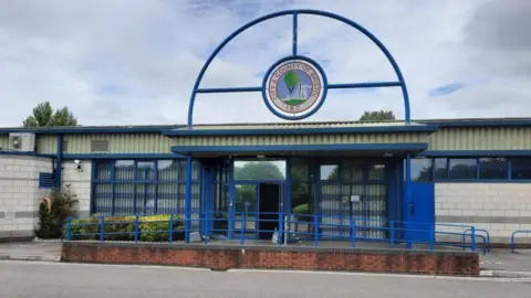 Bristol Indoor Bowls Club The exterior entrance to the Bristol Indoor Bowls Club. There is a ramp leading up to the door with a blue handrail. Above the door there is a large logo of a hot air balloon drifting above the Clifton Suspension Bridge, nestled in a large blue metal arched railing.