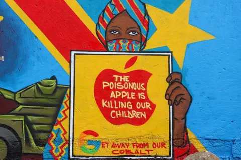 CEM OZDEL / ANADOLU / GETTY IMAGES A painting on a wall shows a woman standing in front of a Congolese flag. She is depicted holding a sign that reads "the poisonous apple is killing our children" and "get away from our cobalt".