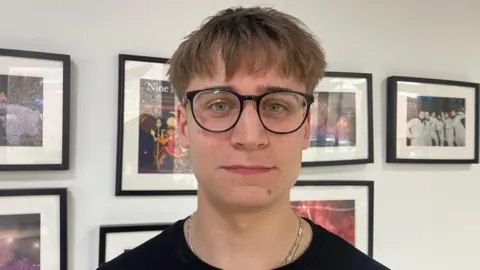 Martim smiling at the camera. He is wearing a black top and round glasses. He has fair hair.