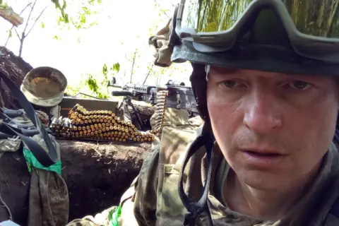 Sergiy Sylantyev Sergiy Sylantyev, a man in Ukraine's military uniform, with a heavy machine gun and ammunition, taking a selfie.