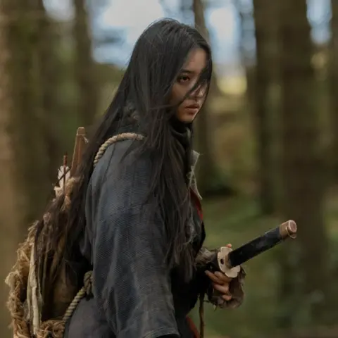 Lionsgate A woman with long black hair and wearing a dark shirt holds a samurai sword