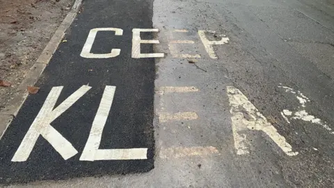 BBC A stretch of newly-patched road covering a "Keep Clear" marking on the road. The repainted marking now reads "Ceep Klear". 