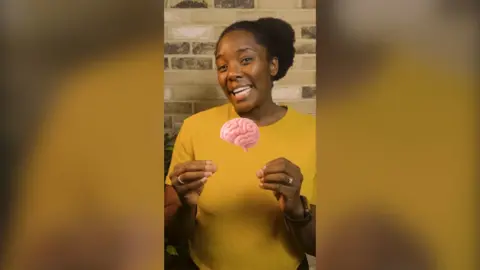 A woman wearing yellow gesticulates with an animation of a brain superimposed