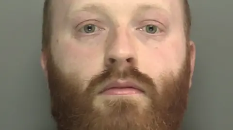 Merseyside Police Daniel Dunne's police mugshot. He has thinning ginger hair and a ginger beard.