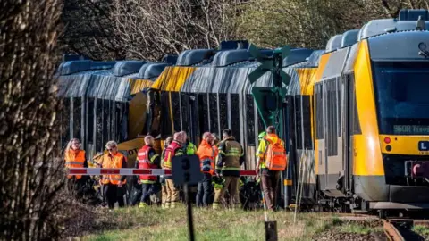 Two trains collided against each other as emergency services stand outside the crash.