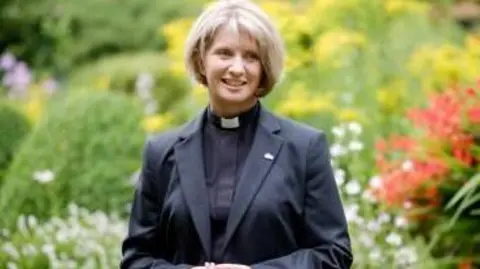 Church of England Bishop of Warrington Bev Mason standing in a garden in front of flowers