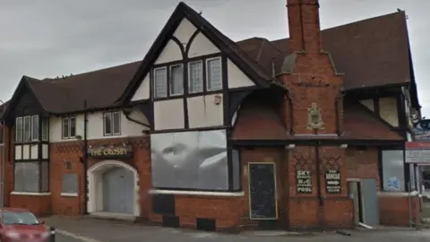 Google view of the Crosby hotel. It is a mock Tudor building, with a steep roof and half-timber framing. Several windows and doors have metal plates fastened on them.