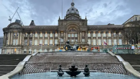 Fountains and steps leading up to the Birmingham City Council building on Victoria Square are in the bottom half of the image. The building with many windows across three levels is in the top half.