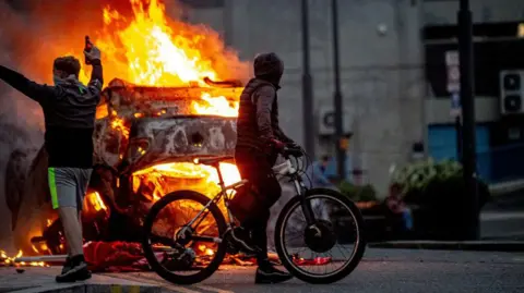 Getty Images Two youths stand in front of a burning vehicle in Sunderland