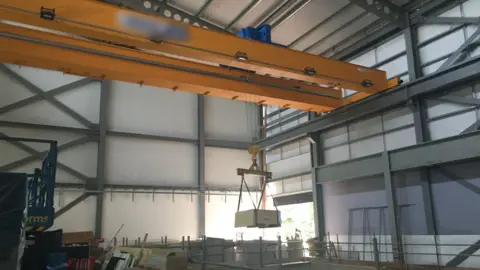 Health and Safety Executive A huge crane in a half-built warehouse at the University of Birmingham. The crane is yellow and materials are hanging in the air. 