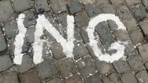 A close up image of the words ING which are painted on cobbles. The leters are smudged and there is bits of paint visible on the stones around 