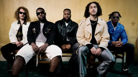 YOUT Five members of Ezra Collective sitting on a bench