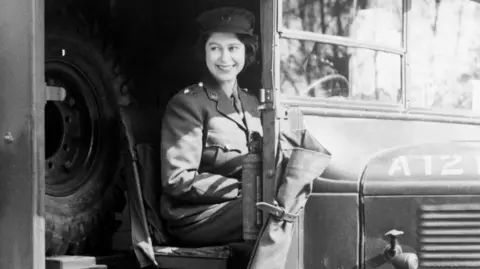 PA Media A black and white image of the Queen sitting in an army jeep wearing the uniform, a khaki shirt and tailored trousers, as she smiles at the camera.