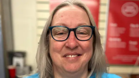 A blonde-haired woman in a blue T-shirt with glasses