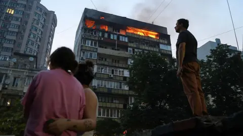 People look at burning apartments in a high-rise residential building hit by Russian shelling on July 10, 2025 in Kyiv, Ukraine.