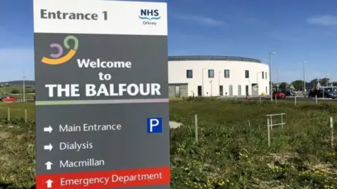 A hospital sign which says 'Welcome to The Balfour', with a hospital building in the background.