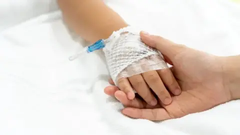 Getty Images A child's hand, swathed in medical bandages, touches an adult's hand against what appears to be a white bedsheet.