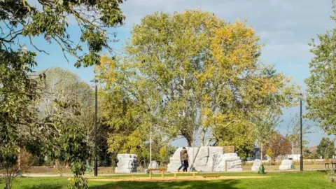 Trees in the new park with two people walking in front of a set of boulders