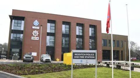 HWFRS A modern-looking brown brick building with lots of tall windows. A sign outside reads "REDDITCH POLICE AND FIRE STATION".