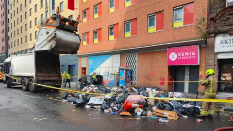 A bin lorry on Glasgow's Jamaica Street, with rubbish tipped out the back. Fire fighters inspect the rubbish. 