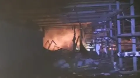 Odesa Dragons Orange flames and smoke can be seen in the far off distance inside what was the boat club. Racks that contained boats on one side have been damaged or burnt with collapsed structures in the foreground