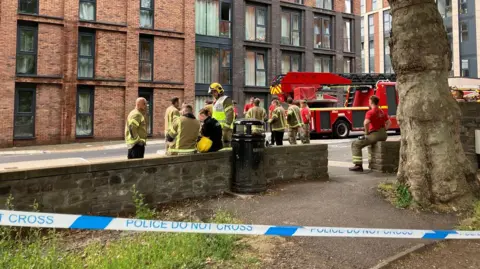 Several firefigthters and a fire engine outside of a tower block in Bristol City Centre. The area is cordoned off with police tape.