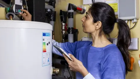 Woman turning down her thermostat at her home in the North East of England