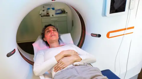 The image shows a female patient lying during CAT scan. Mature hispanic woman going through MRI scanner in examination room at hospital.