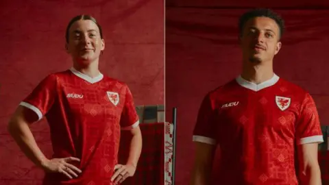 Angharad James-Turner and Ethan Ampadu stand side by side in a split portrait against a deep red backdrop, each wearing a bright red football shirt with white trim and a white crest featuring a red dragon on the chest. The shirt has a patterned design woven into the fabric. Angharad James-Turner on the left is shown from the waist up with one hand on her hip, while Ethan Ampadu faces the camera with their arms down. Studio lighting highlights the new team kit, with matching red tones throughout the image.