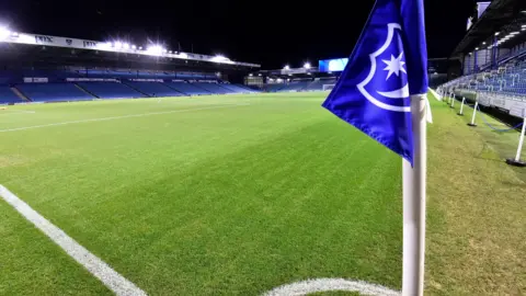 Rex Features Portsmouth's club badge on a corner flag at Fratton Park. It is a wide shot of the pitch and stands under floodlights, but without any fans present.