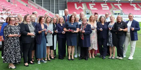 PA Media Picture of Prince William with a number of the Welsh women's rugby team, smiling and holding their caps at the Parc Y Scarlets stadium. 