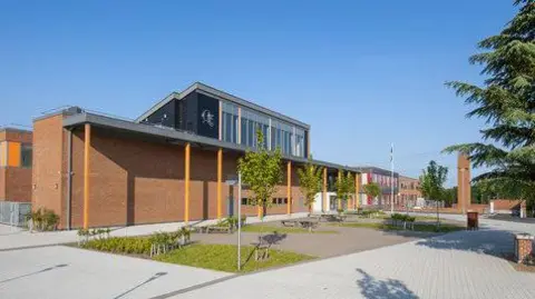 QE School Exterior of QE School. A long modern red-brick building with a canopy running along the front and a black rendered first floor with large windows