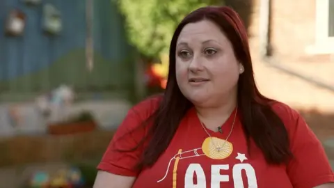 BBC/The One Show Elli has long dark-red hair and wears a red T-shirt with the AFO logo on it. She is sitting outside for her TV interview.